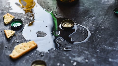 Spilled drink pooling on a dark table among bottle caps and crackers