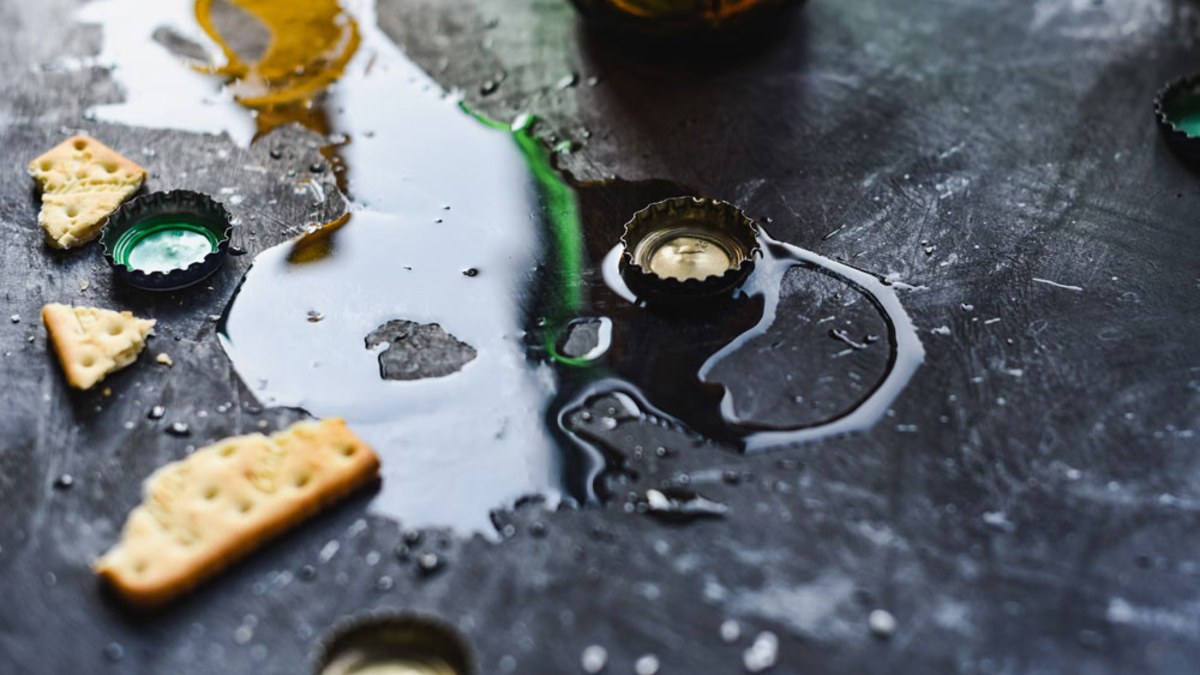 Spilled drink pooling on a dark table among bottle caps and crackers