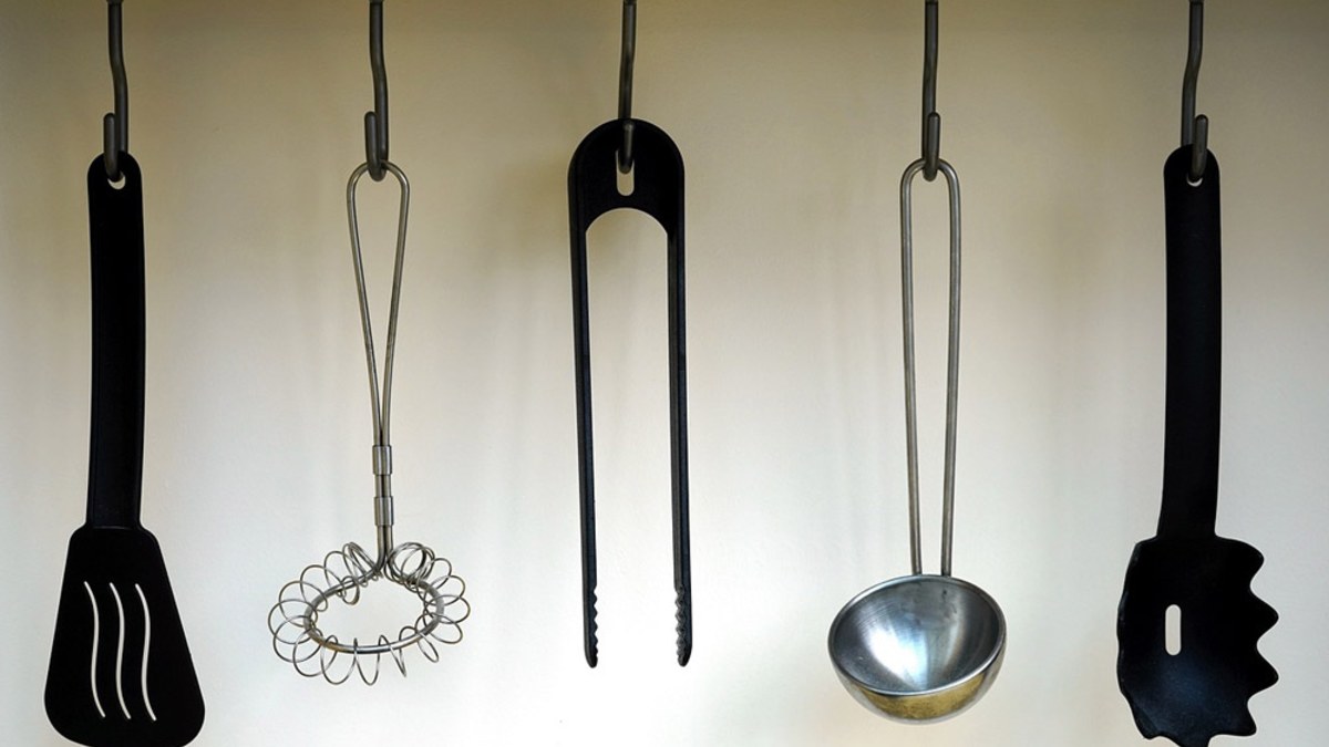 Black nylon spatula, tongs and pasta server hanging on a rail with a whisk and ladle