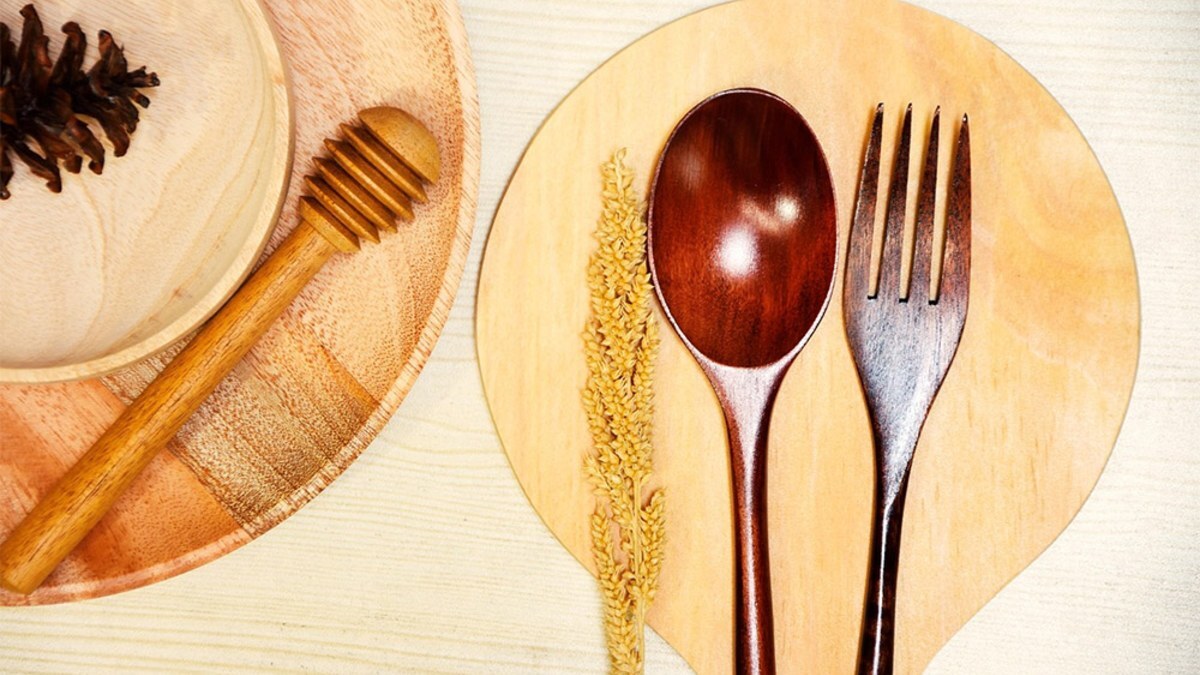 Wooden spoon and fork on a wooden plate beside a honey dipper, seen from above