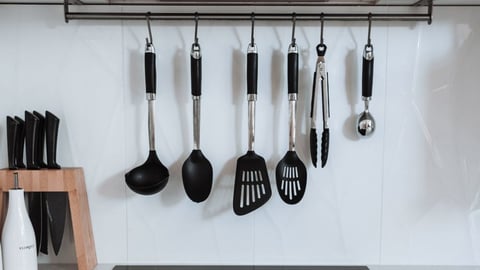 Black cooking utensils hanging from a rail above a cooktop in a white kitchen