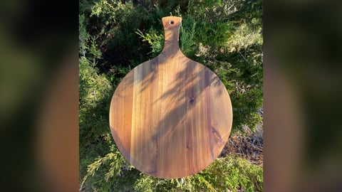 Round acacia wood paddle board propped against evergreen shrubs in the sun