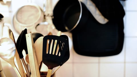Holder of black and stainless steel cooking utensils in a white-tiled kitchen