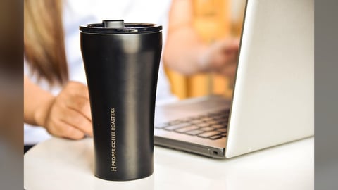 Black insulated tumbler on a desk beside a laptop