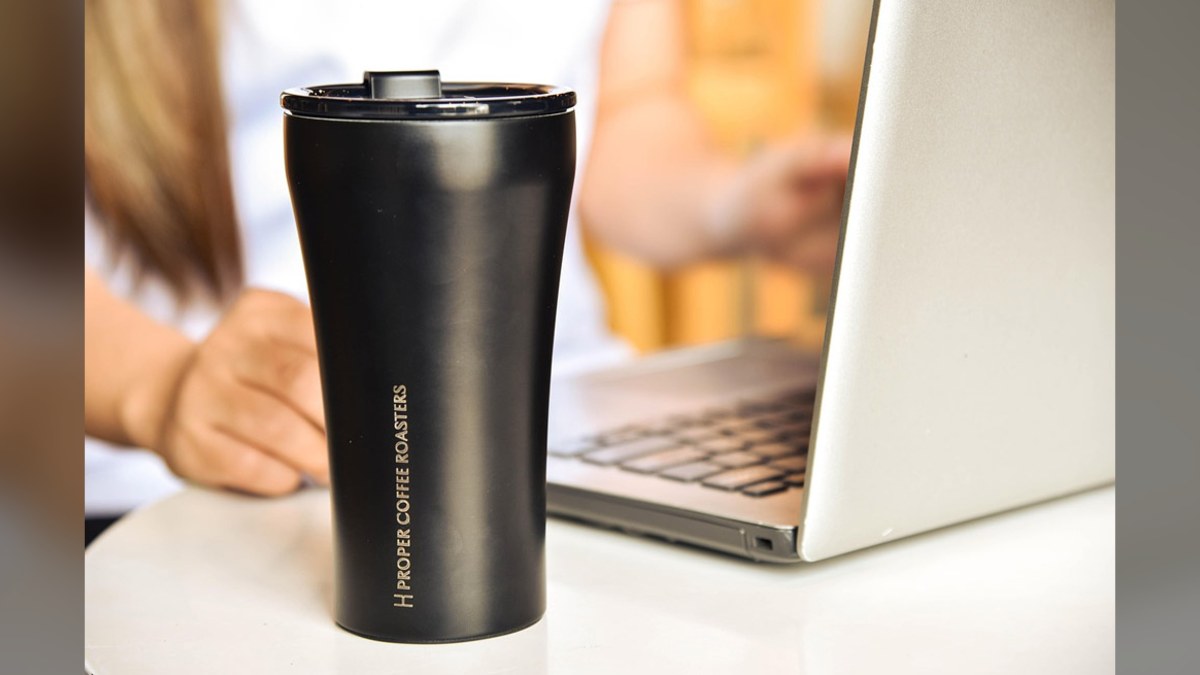 Black insulated tumbler on a desk beside a laptop