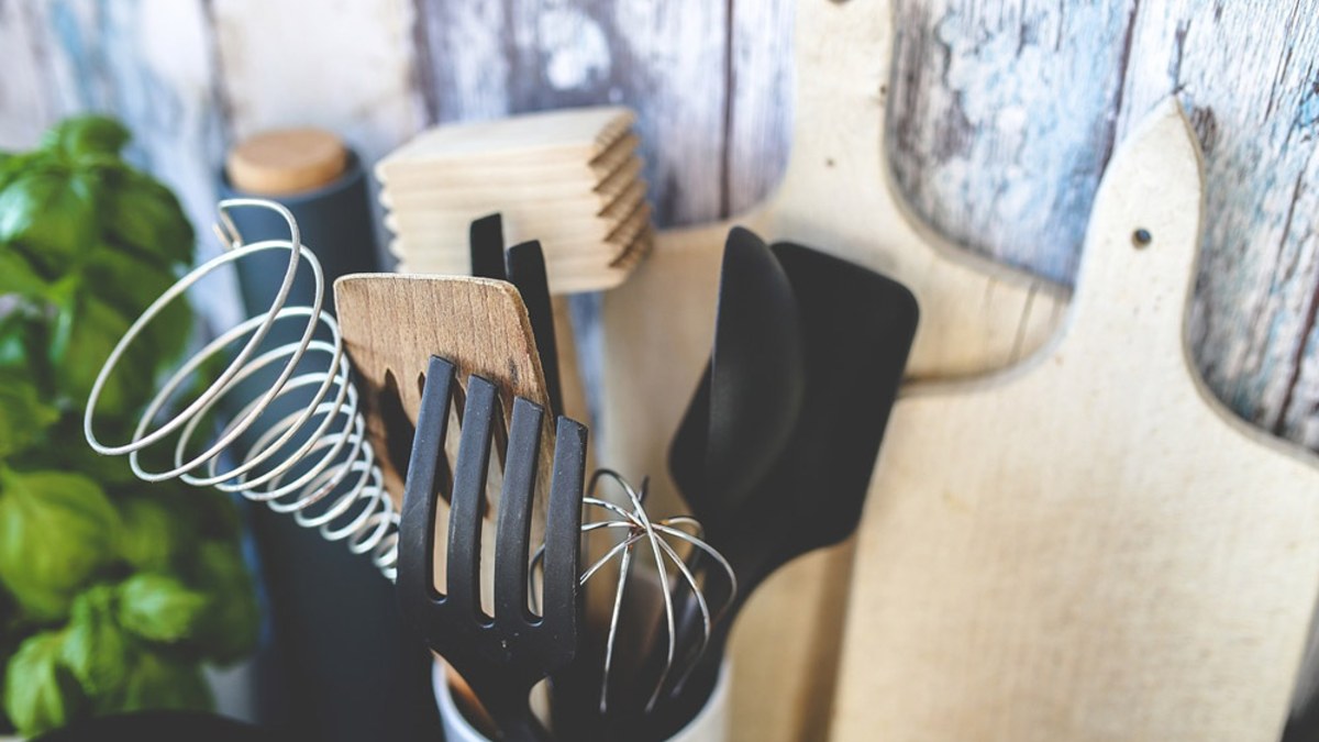 Whisks, spatulas and a wooden meat tenderizer in a holder beside wooden cutting boards and a basil plant