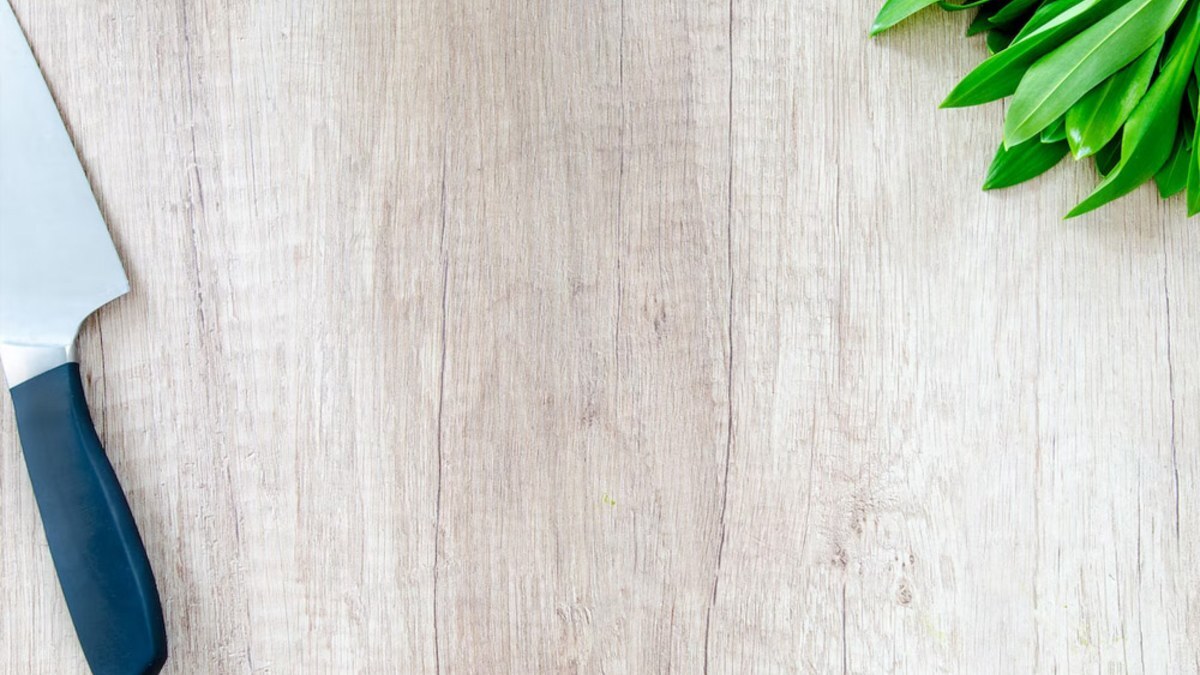 Chef's knife and fresh greens on a light wood surface