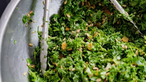 Metal tongs tossing chopped kale in a large bowl
