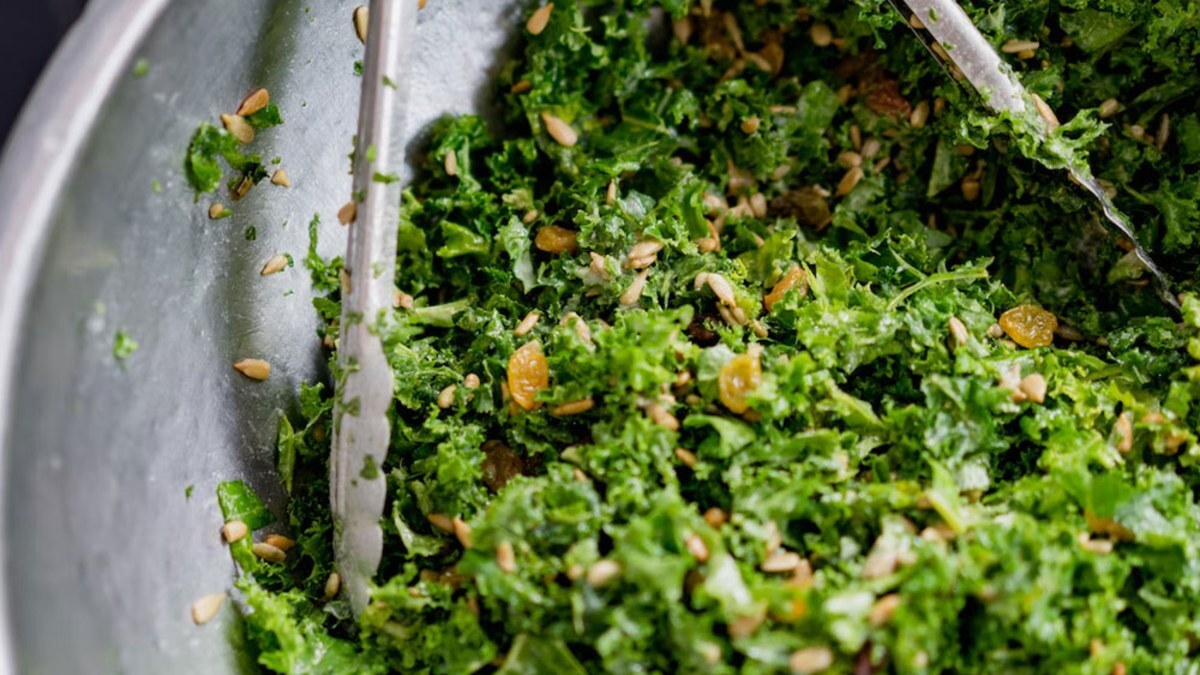 Metal tongs tossing chopped kale in a large bowl