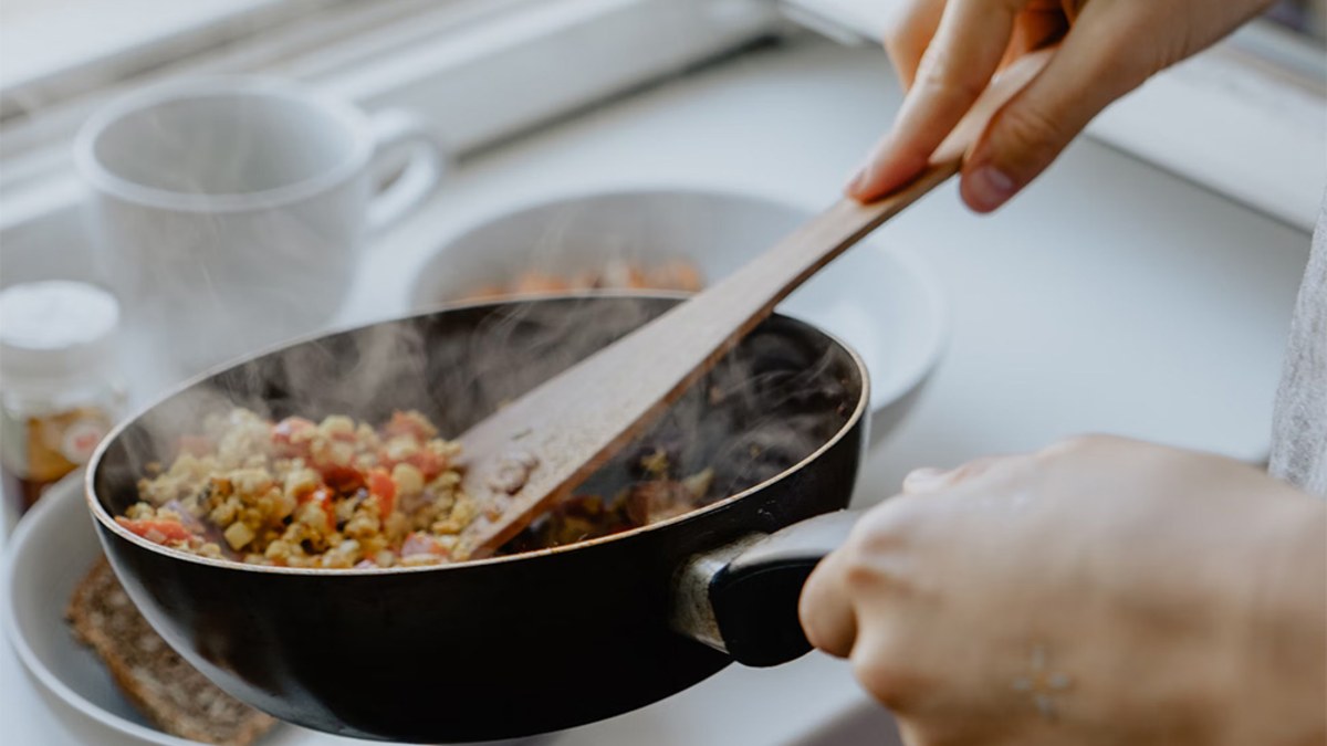 Hands stirring a steaming pan of fried rice with a wooden spatula