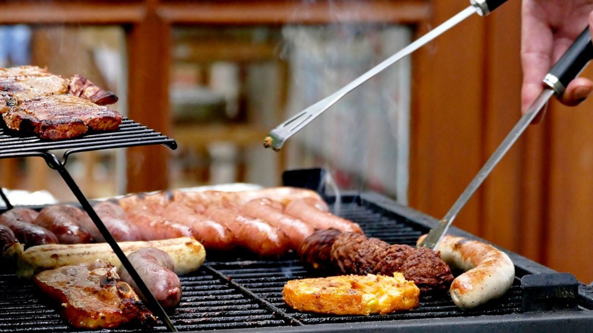 Sausages, steak and chicken on a grill being turned with long metal tongs