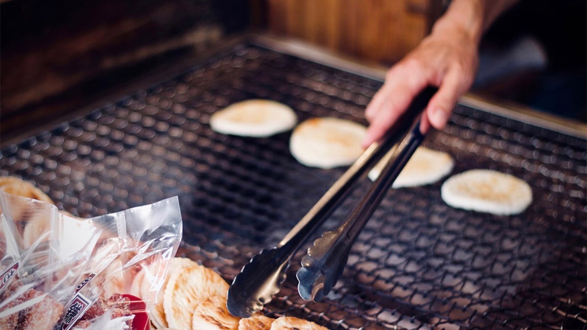 Metal tongs turning rice cakes on a hot grill grate