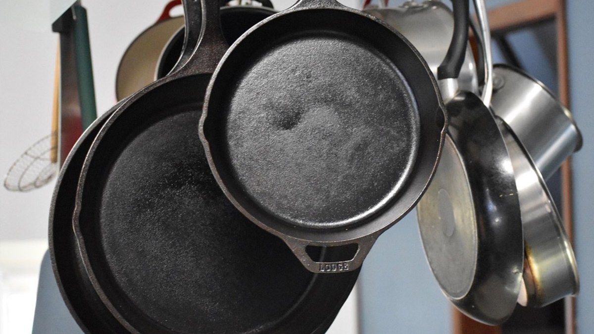 Cast iron skillets and stainless steel pans hanging from a kitchen rack