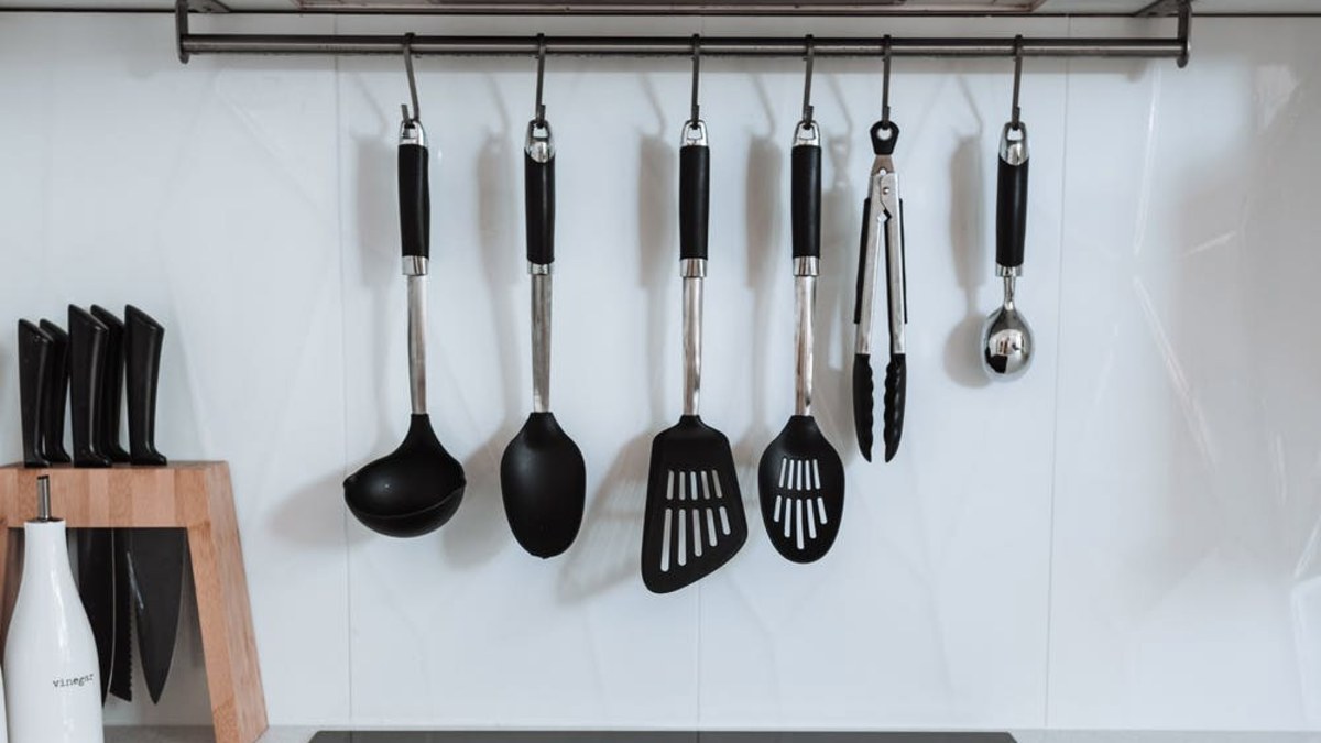 Black cooking utensils hanging from a rail above a cooktop in a white kitchen