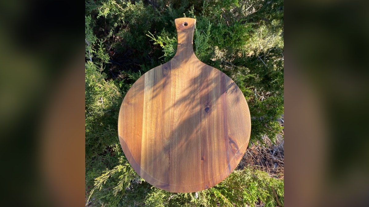 Round acacia wood paddle board propped against evergreen shrubs in the sun