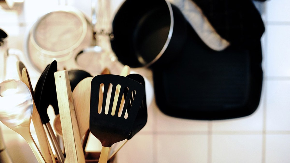 Holder of black and stainless steel cooking utensils in a white-tiled kitchen