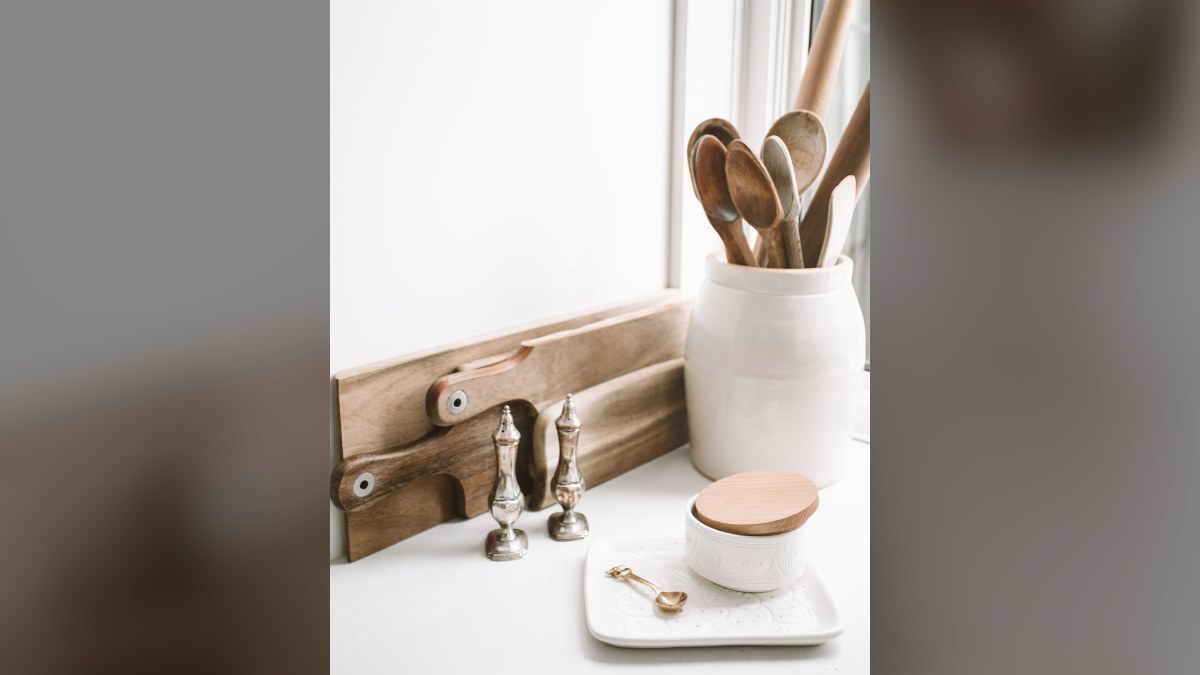 Wooden spoons in a white crock beside wooden boards and salt and pepper shakers