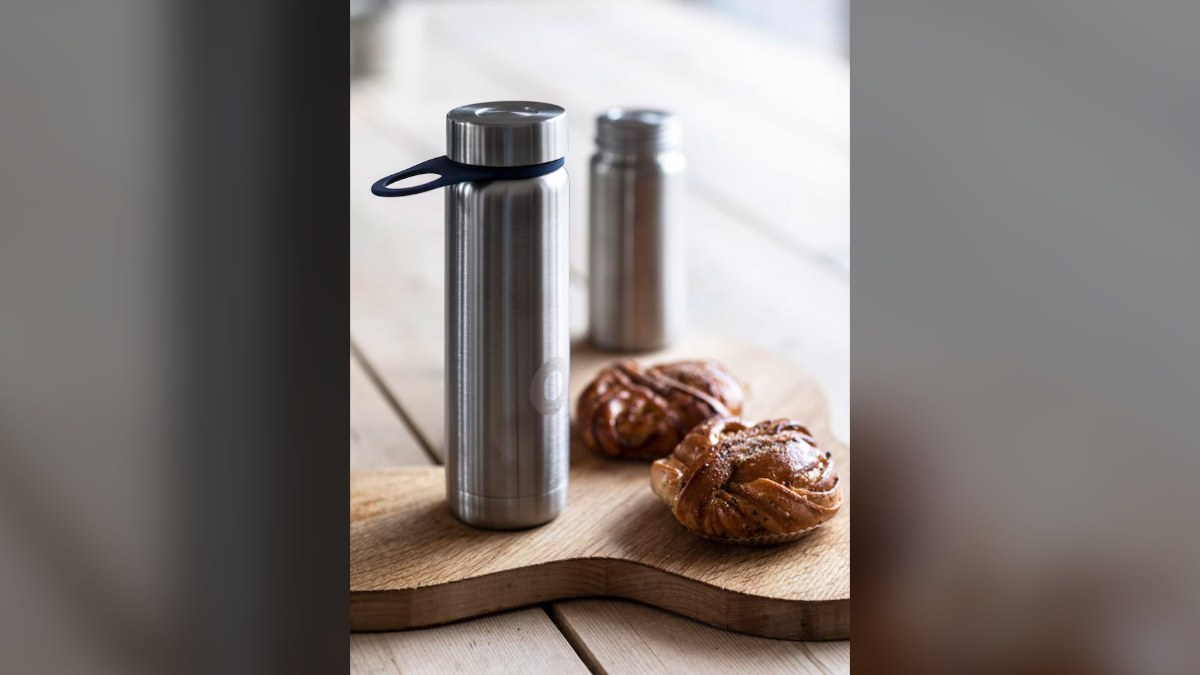 Two stainless steel insulated bottles on a wooden board next to cinnamon buns