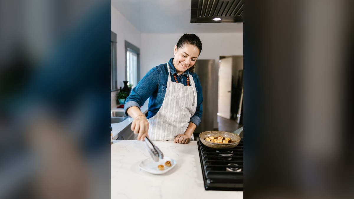 Smiling cook in a striped apron plating food with tongs at a kitchen counter