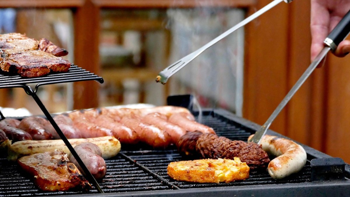 Sausages and chicken on a grill being turned with long metal tongs